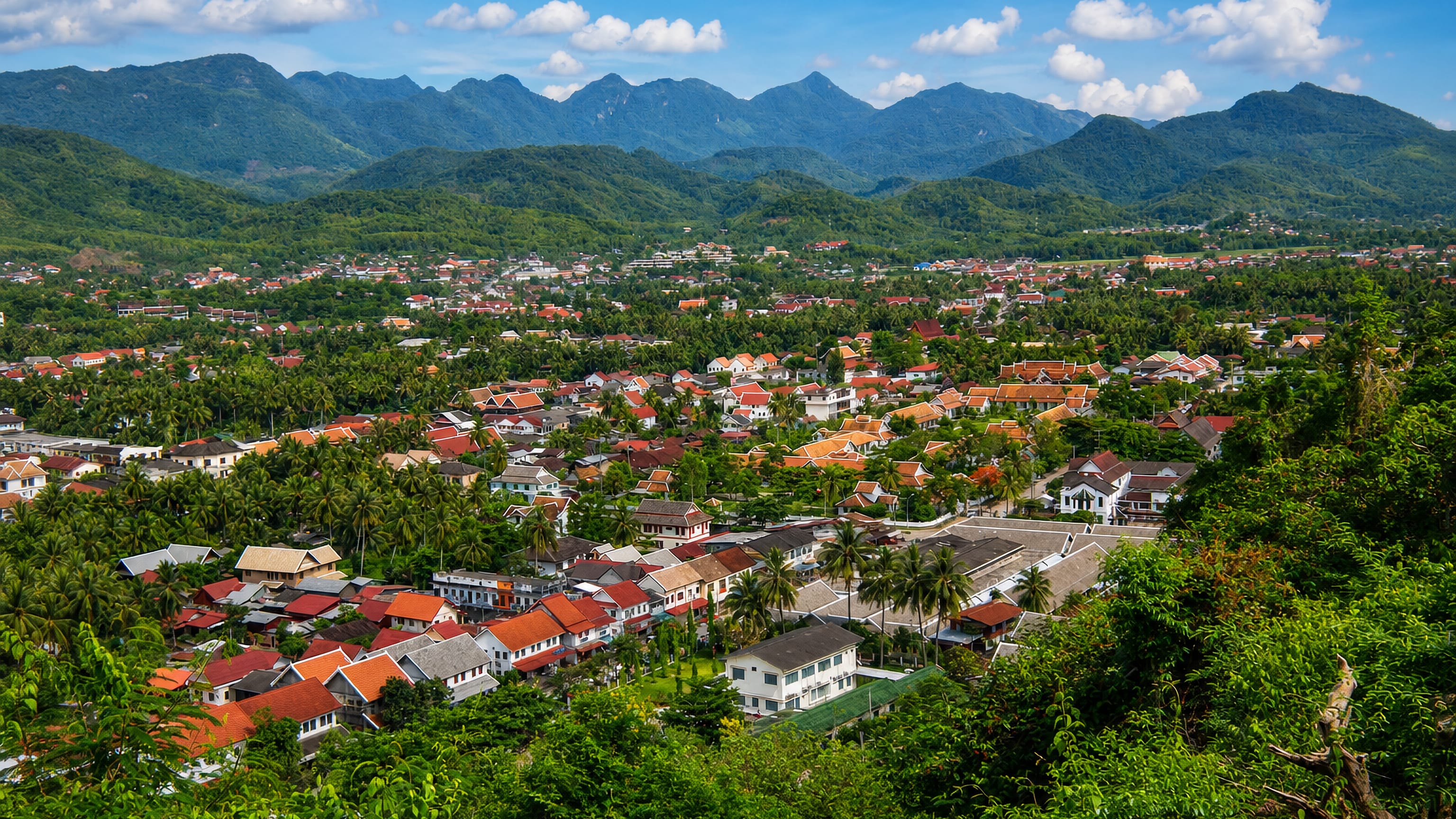 Red-tiled roofs and palms of Luang Prabang spread across the valley below forested Lao mountains
