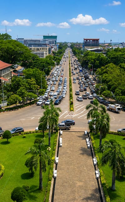 View from Patuxai monument down a palm-lined avenue over Vientiane's traffic and low-rise skyline