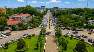 View from Patuxai monument down a palm-lined avenue over Vientiane's traffic and low-rise skyline