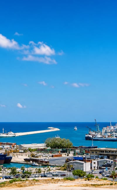The Port of Beirut with grain silos, cranes and container ships along the Mediterranean under clear skies.