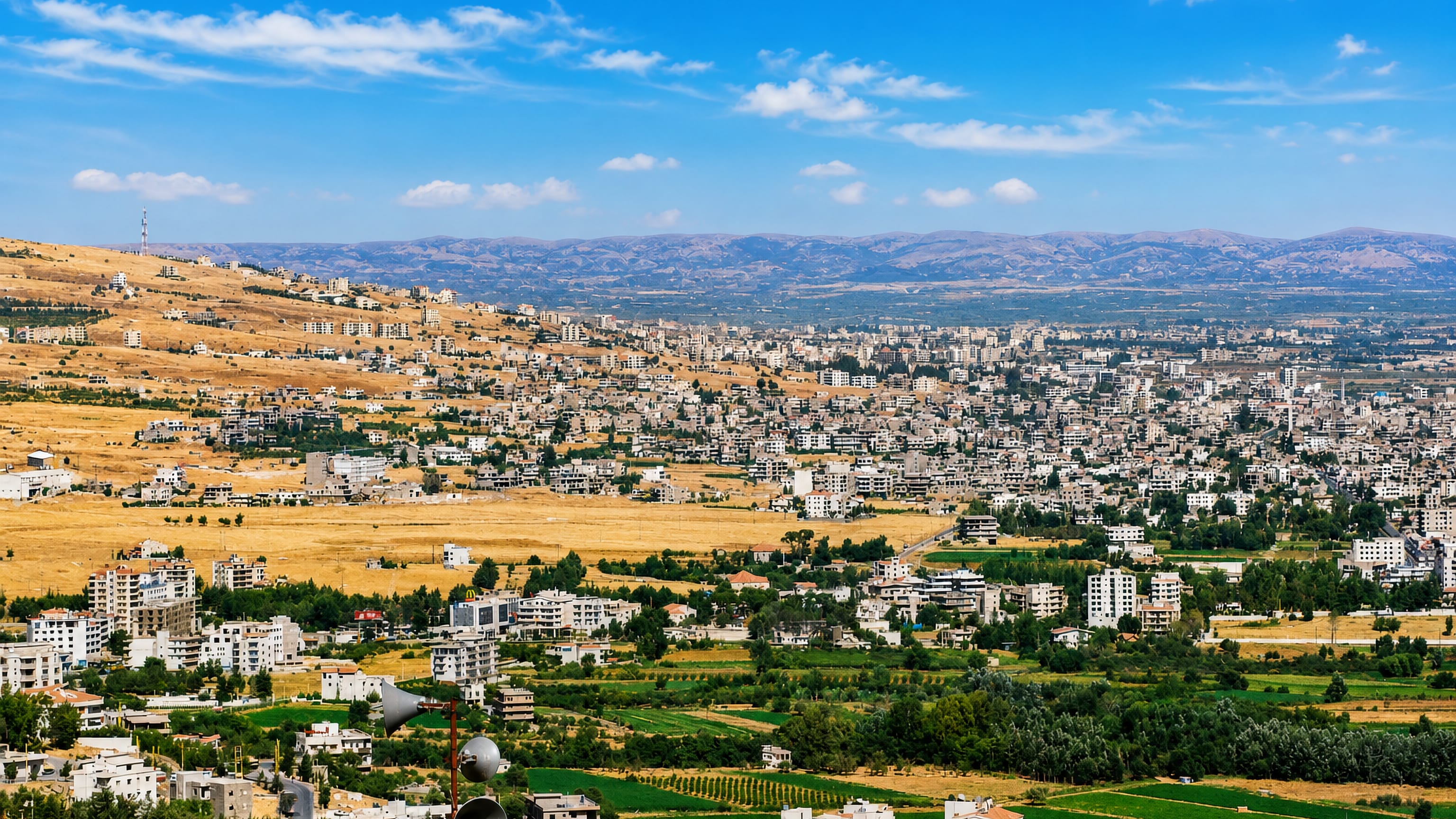 Zahle, Lebanon climbing the dry Bekaa hillside above green vineyards and cultivated fields.