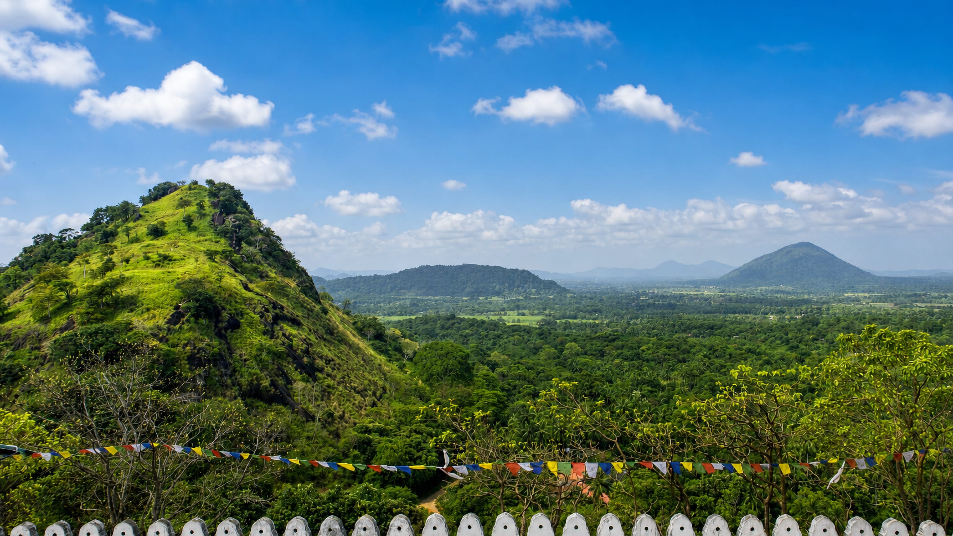 Green rock hill and forested plains seen from a hilltop Buddhist terrace with prayer flags in Dambulla, Sri Lanka