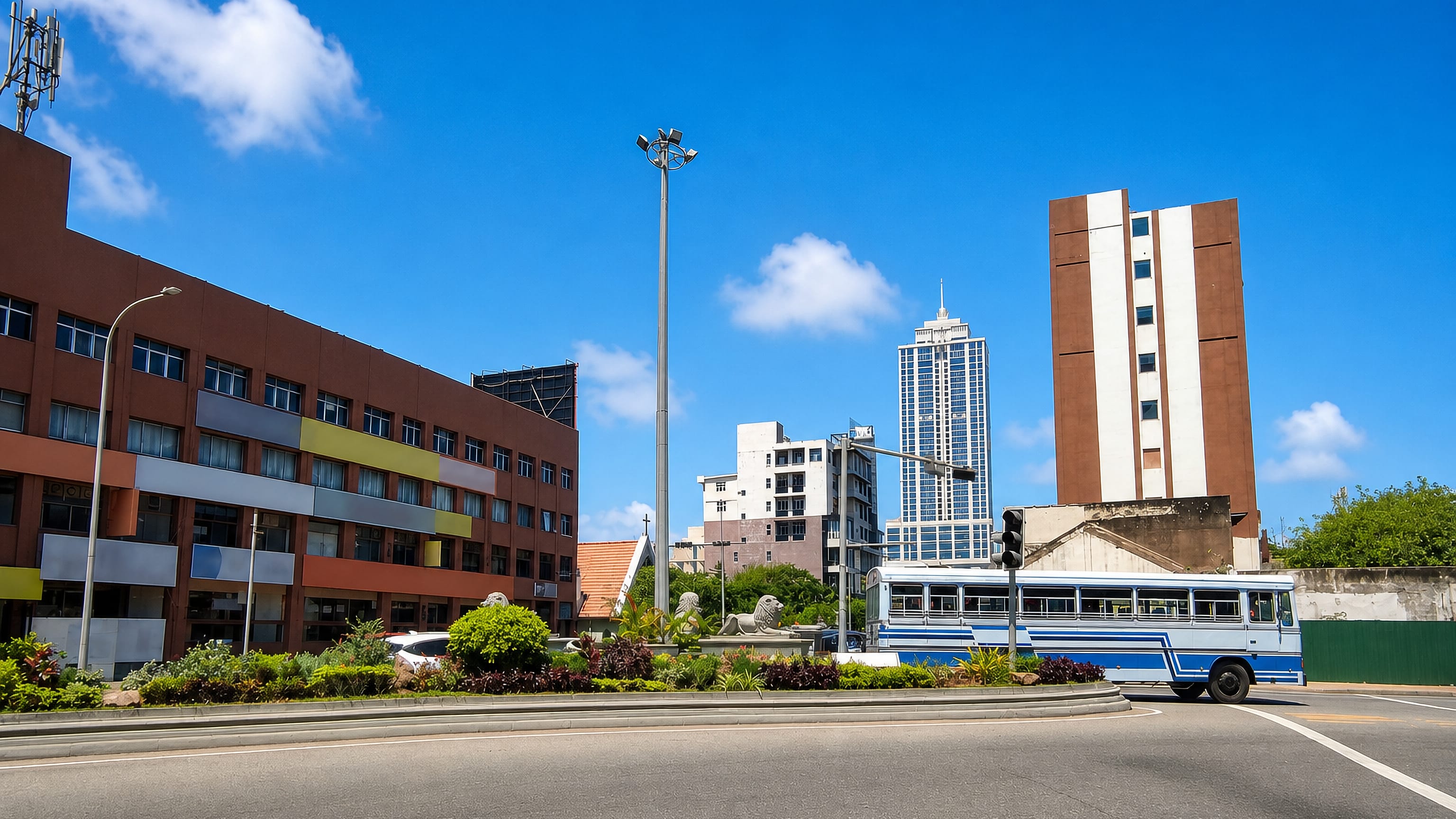 Blue bus, lion statues and mid-rise towers along a wide sunlit road in Kollupitiya, Colombo.