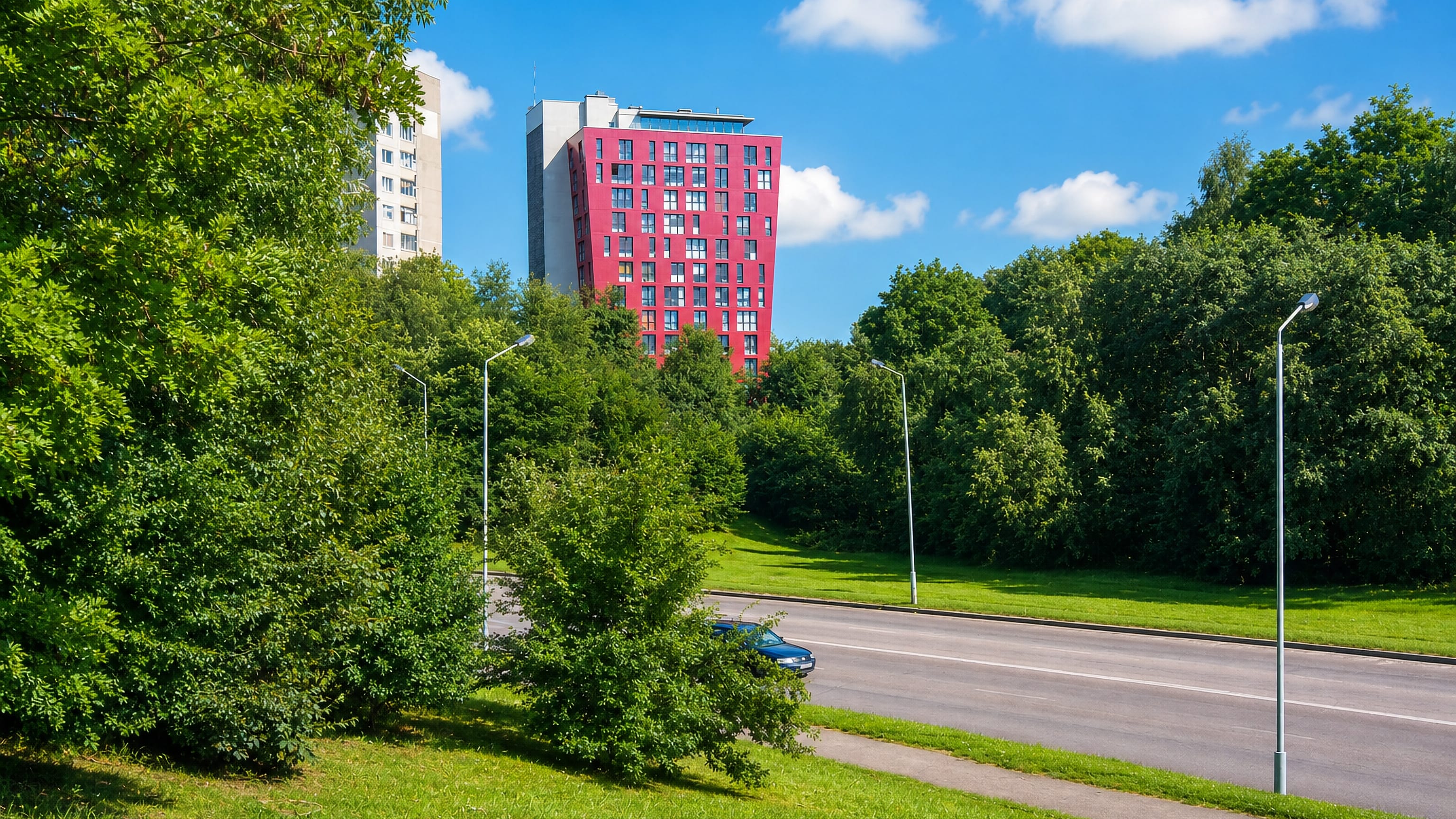 A crimson high-rise and Soviet-era apartment blocks rising above tree-lined green verges in Eiguliai, Kaunas.
