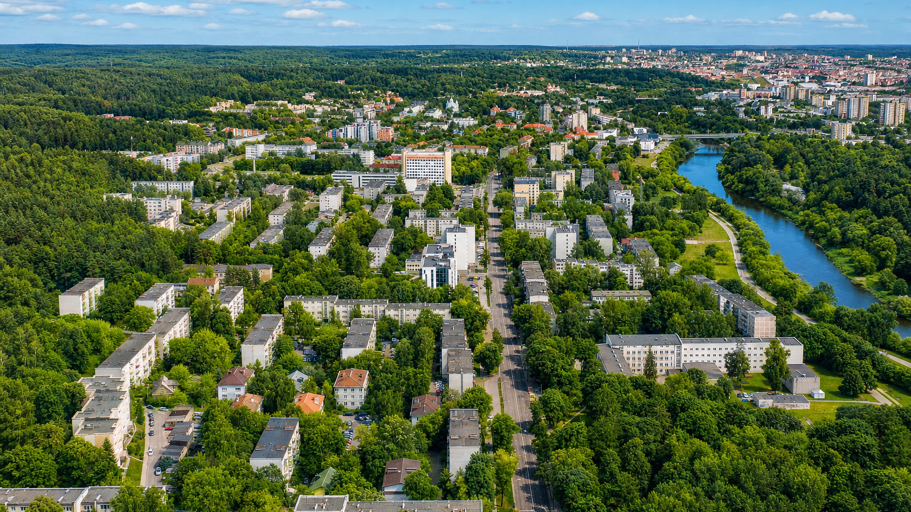 Aerial over Antakalnis in Vilnius, low apartment blocks in dense greenery beside a bend of the Neris.