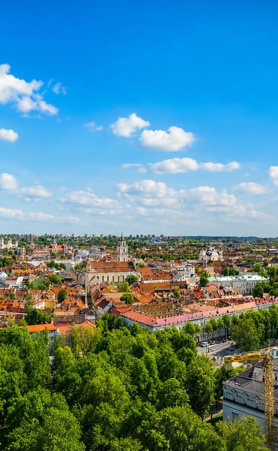 Vilnius Old Town panorama with red-tiled roofs and church spires under a blue sky, seen from Gediminas Hill.