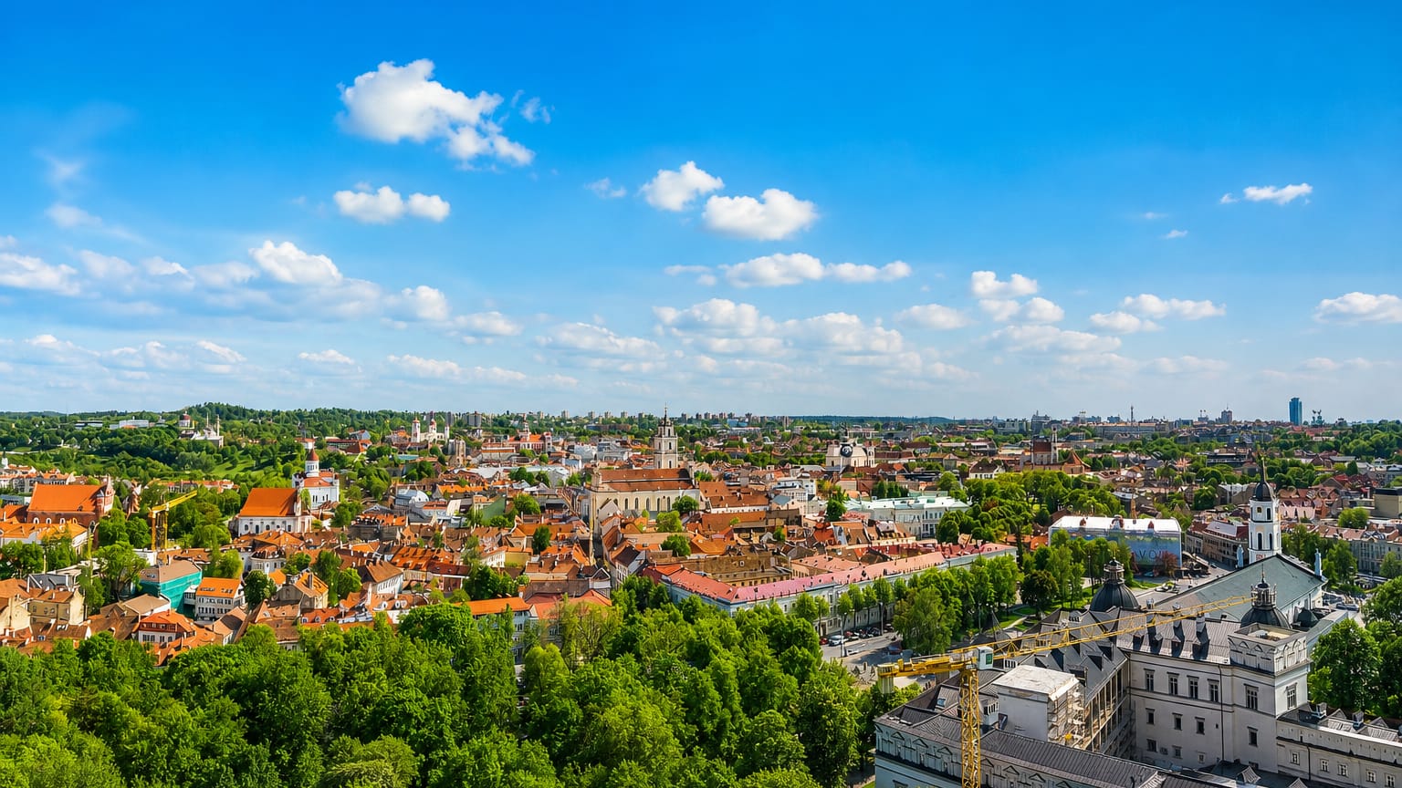 Vilnius Old Town panorama with red-tiled roofs and church spires under a blue sky, seen from Gediminas Hill.