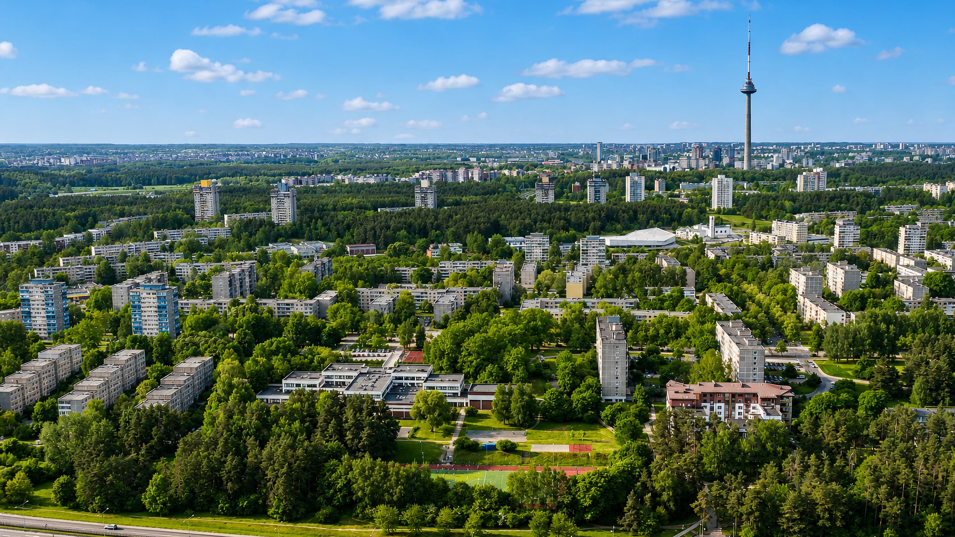 Aerial view of Lazdynai's modernist apartment blocks among pine woods with the Vilnius TV Tower beyond.