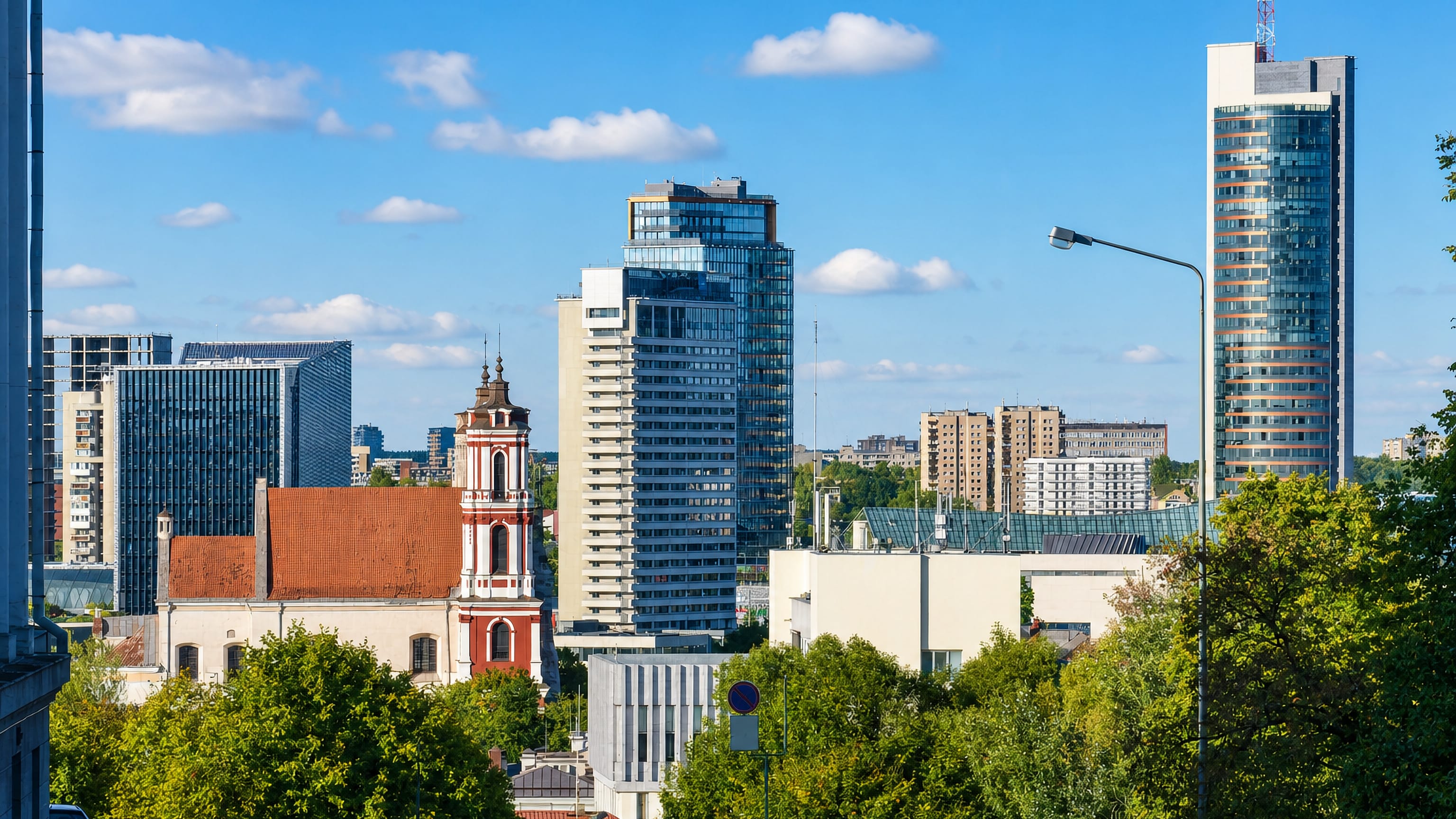 Naujamiestis skyline in Vilnius, a baroque church tower standing against glass high-rises above leafy streets