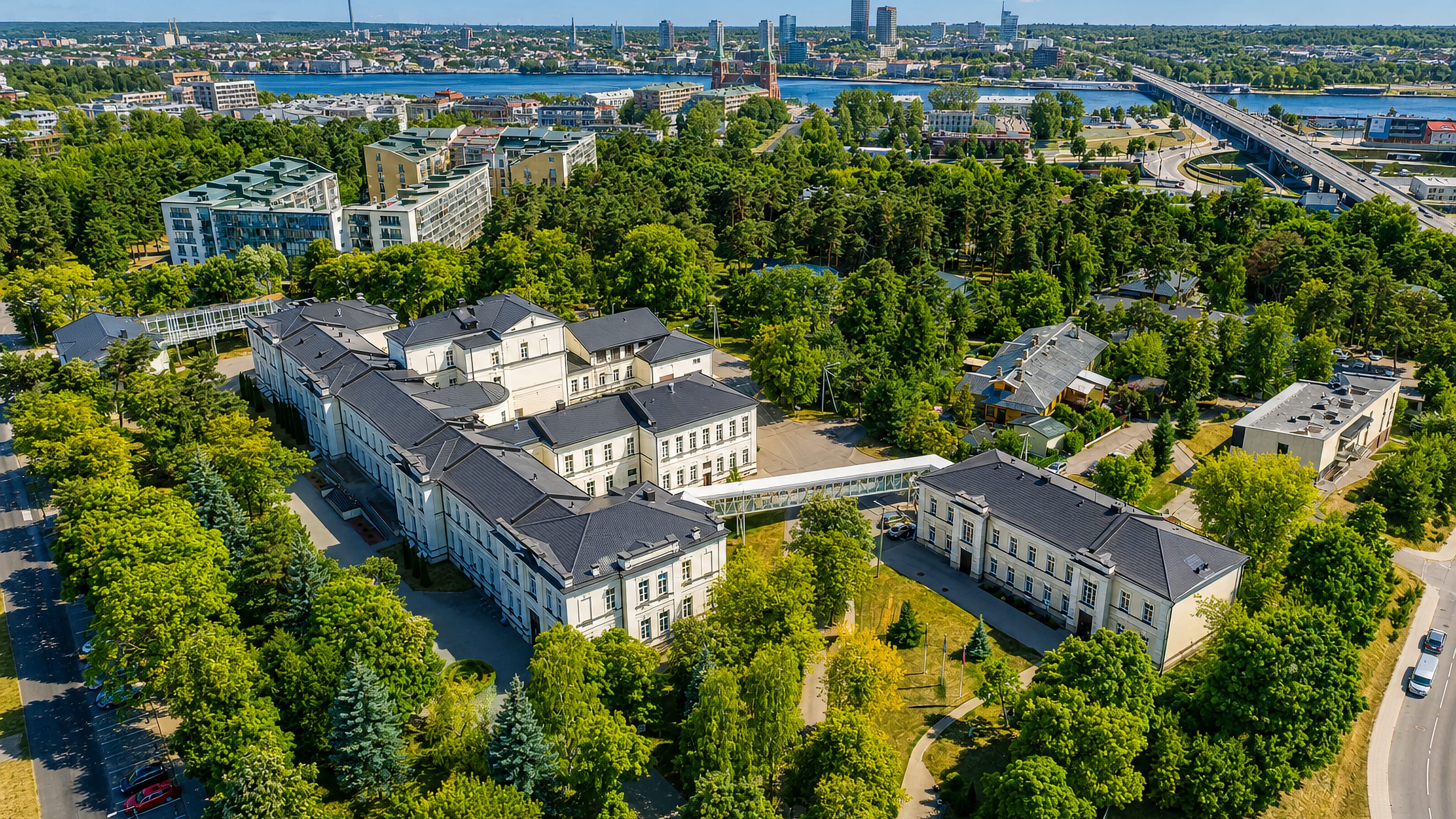 Aerial view over Vilkpėdė's wooded blocks in Vilnius toward the Neris, the TV Tower and the city's towers