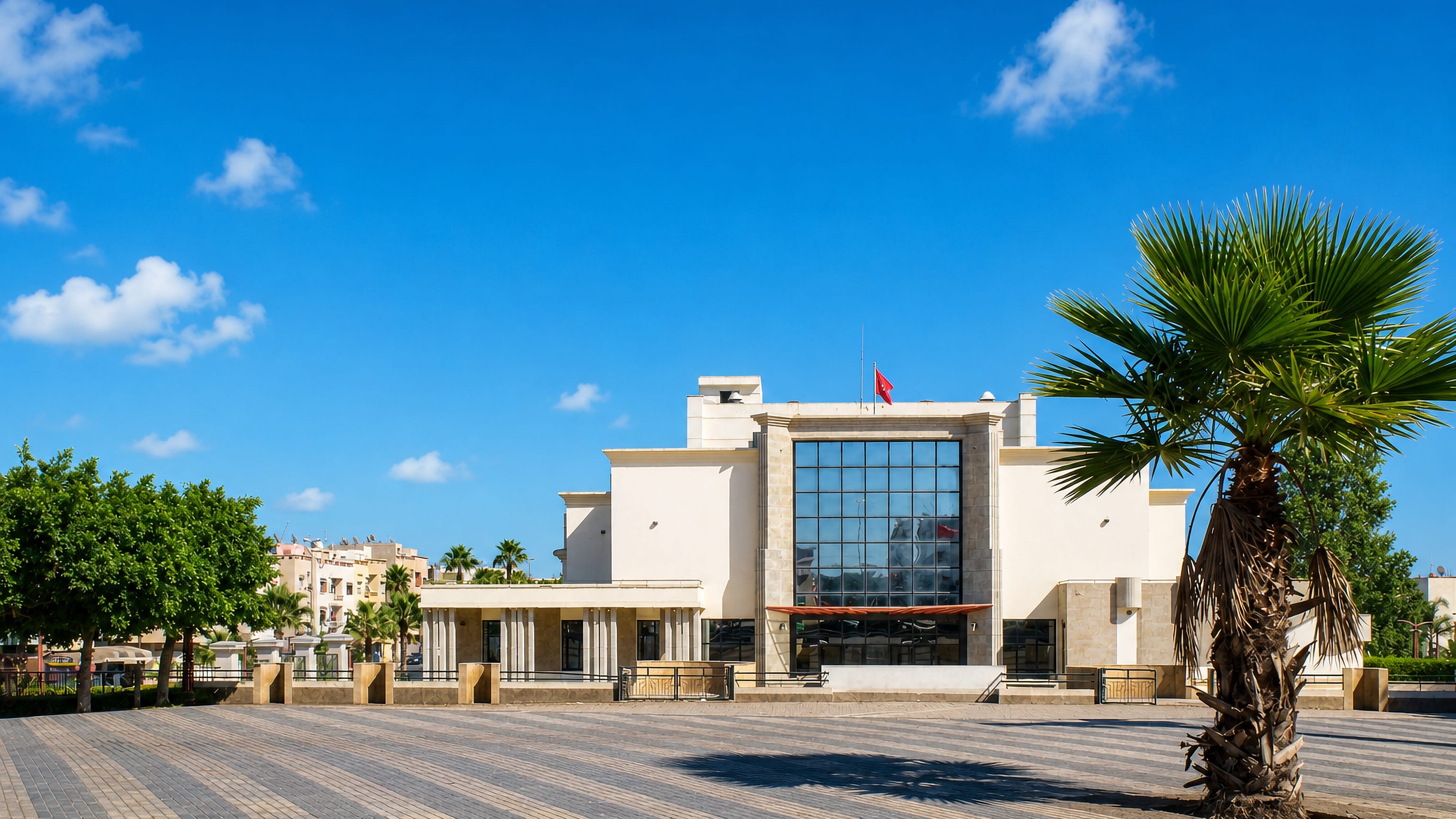 White modernist civic building flying a Moroccan flag across a wide paved plaza in Mohammedia, Morocco.