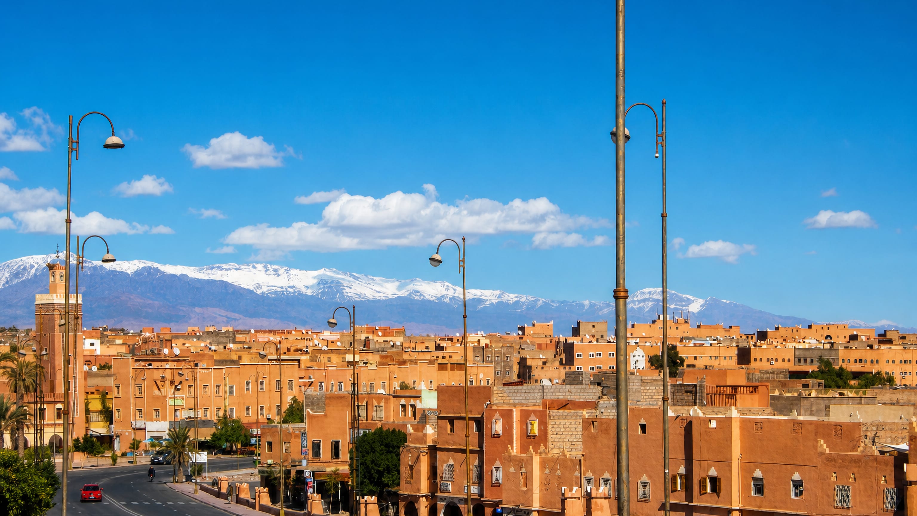 Ouarzazate's ochre kasbah buildings and minaret line a wide boulevard beneath the snow-capped High Atlas.