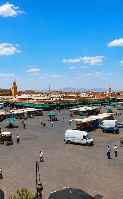 Marrakesh's Jemaa el-Fnaa square with market stalls, horse carriages, red medina walls and a minaret under a bright sky