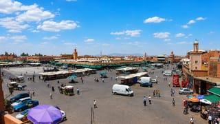 Marrakesh's Jemaa el-Fnaa square with market stalls, horse carriages, red medina walls and a minaret under a bright sky