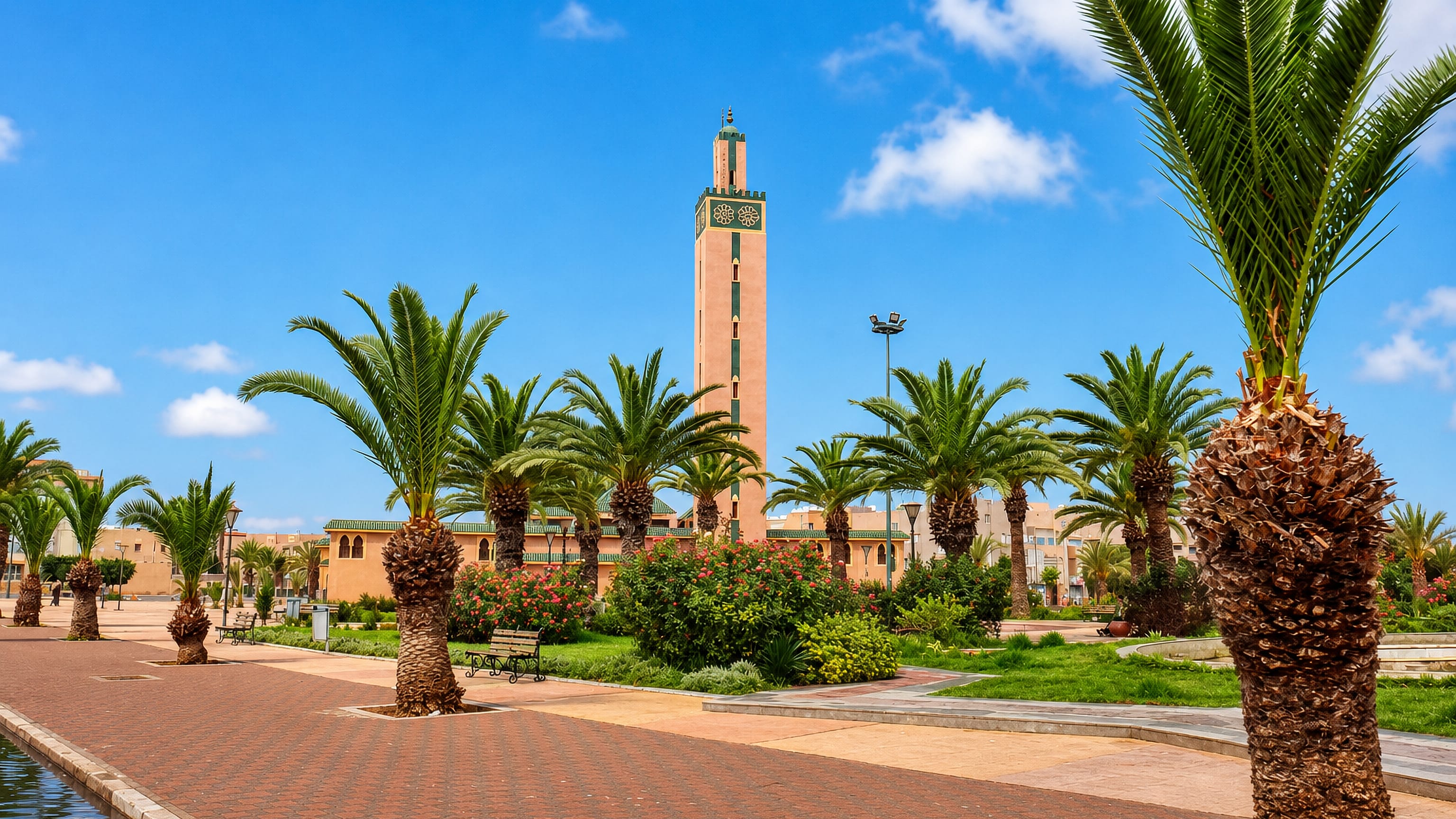 Palm-lined promenade and an ochre mosque minaret in Tiznit, Morocco, under a clear blue sky.