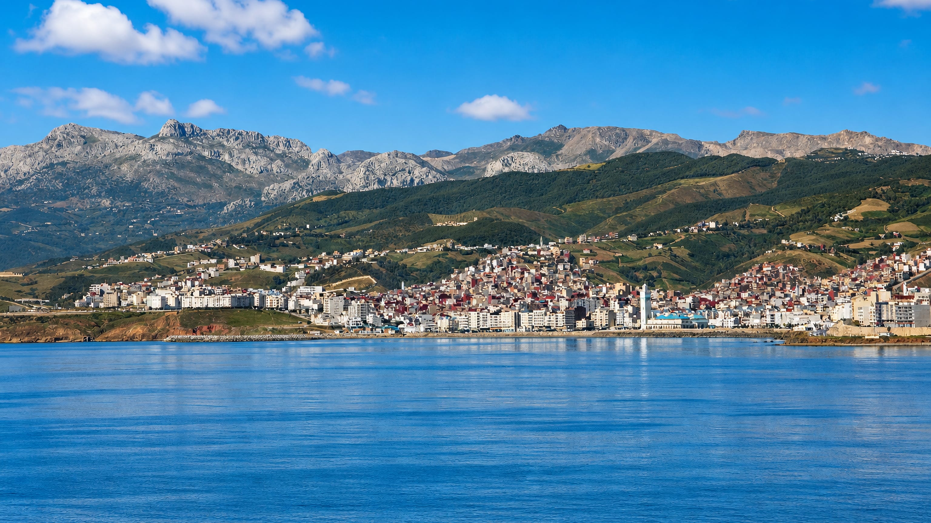 Fnidek's white seafront town rising to the Rif mountains, seen across the calm Mediterranean.