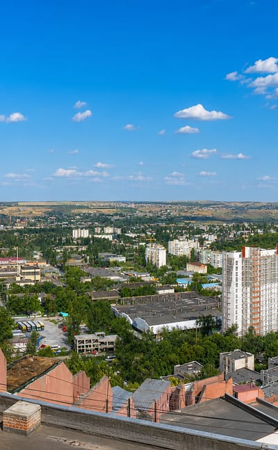 View across Chisinau's tree-lined residential blocks toward rolling hills under a blue summer sky.