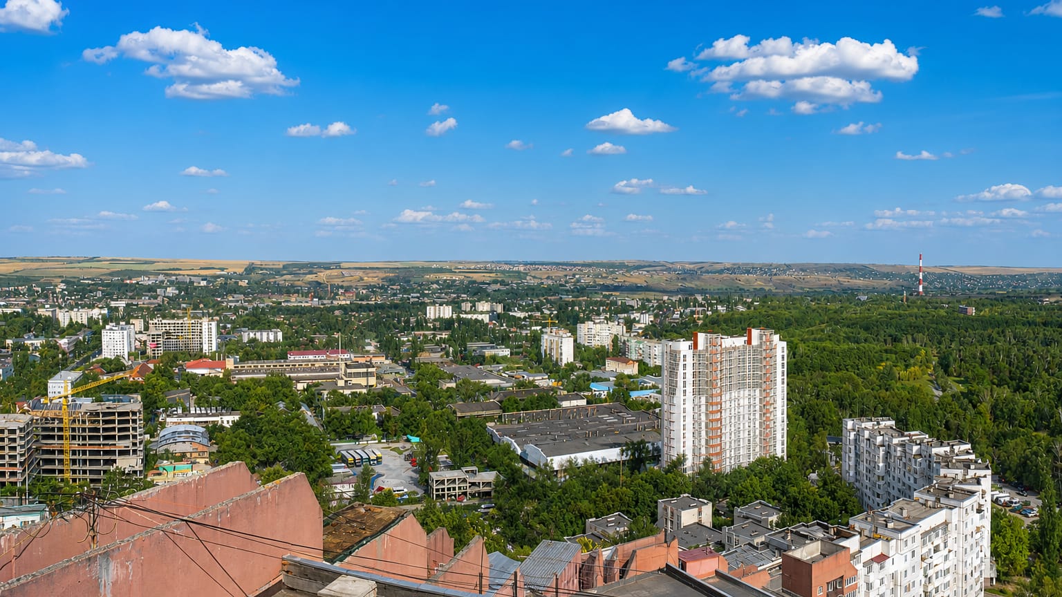 View across Chisinau's tree-lined residential blocks toward rolling hills under a blue summer sky.