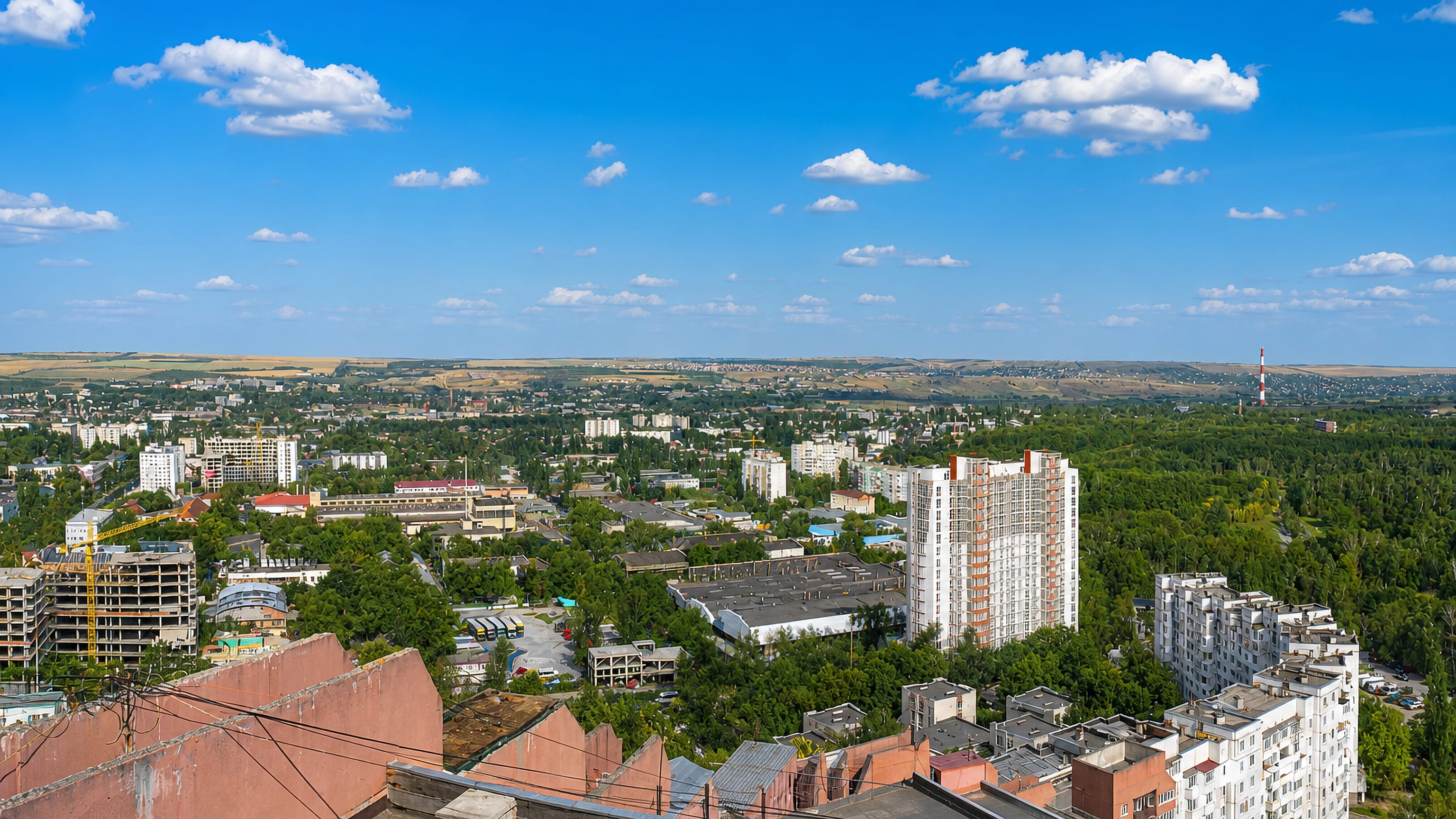 View across Chisinau's tree-lined residential blocks toward rolling hills under a blue summer sky.