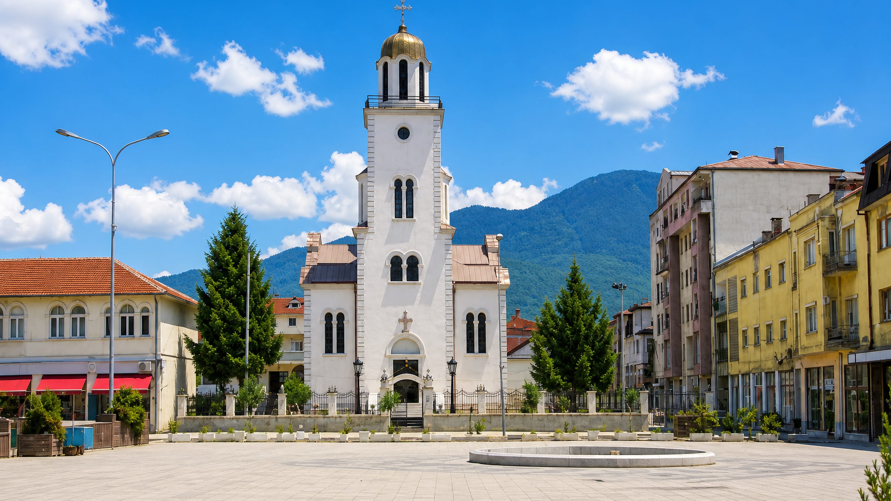 Paved main square with a gold-domed white Orthodox church below the mountains in Gostivar, North Macedonia.