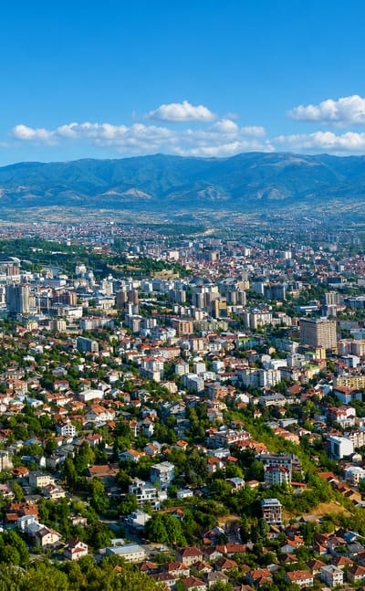 Panorama of Skopje spread across its valley with the surrounding mountains under a blue sky