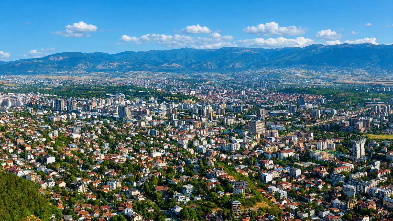 Panorama of Skopje spread across its valley with the surrounding mountains under a blue sky