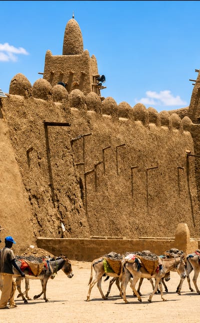 The mud-brick Djinguereber Mosque in Timbuktu with a donkey caravan crossing the sandy square.