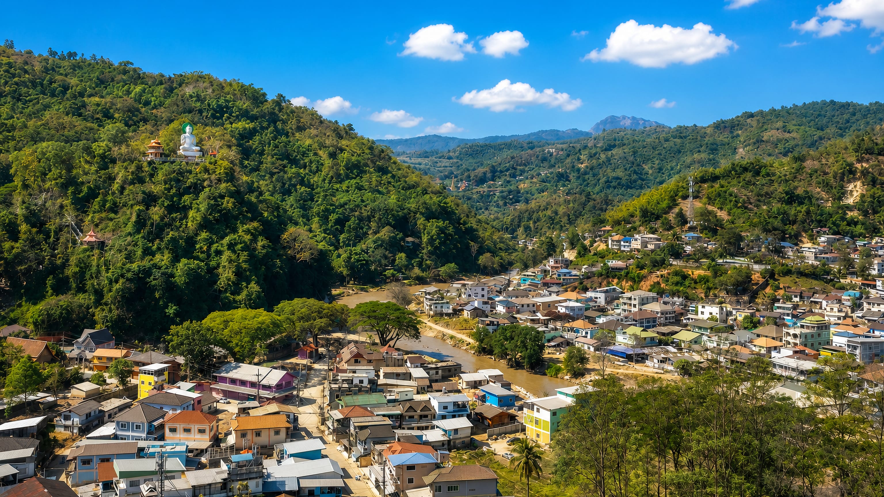 Tachilek, Shan State, spread along the border river below forested hills crowned by a white Buddha statue.