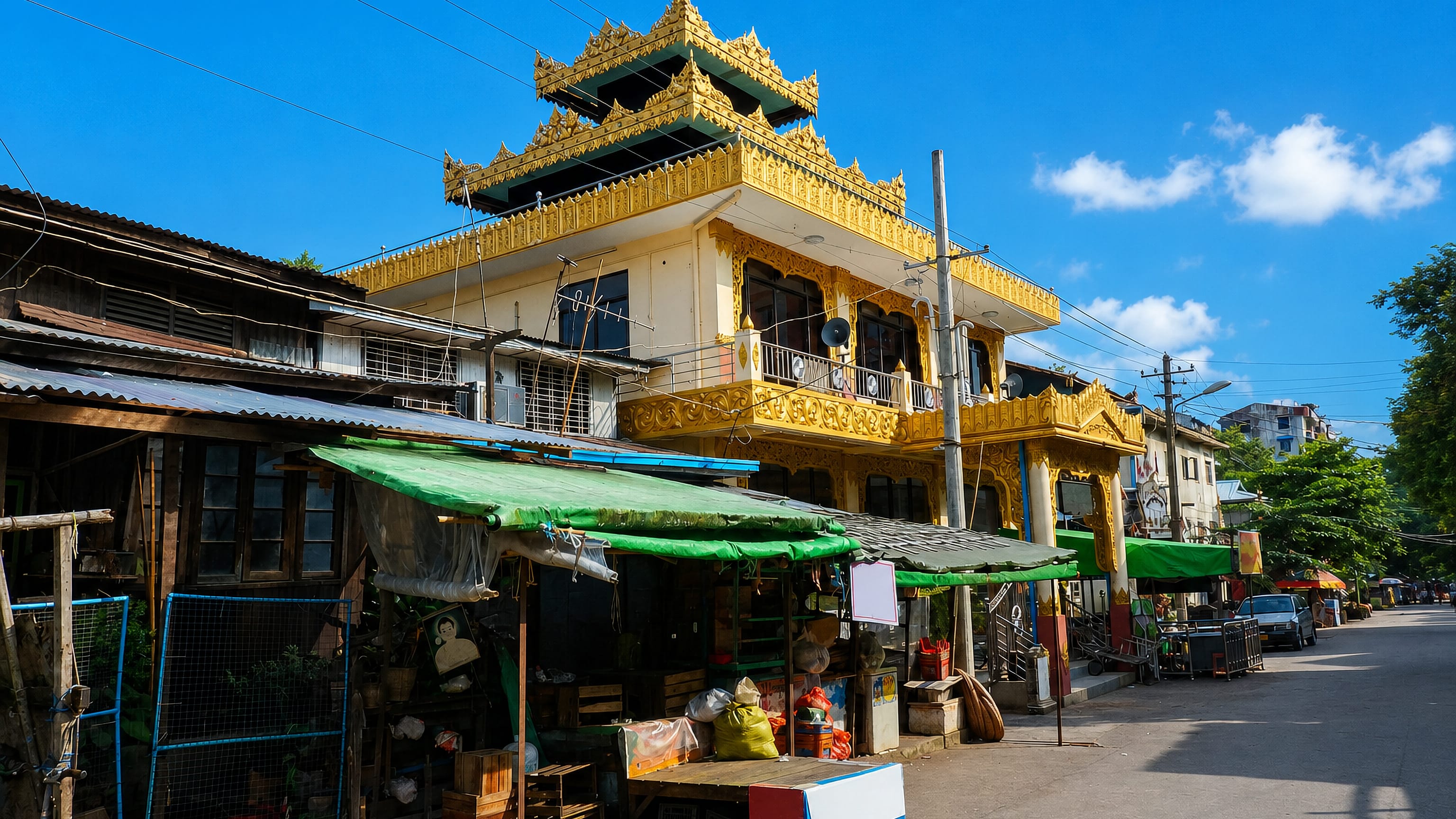 Gold-tiered monastery rising above street-market stalls in Kyimyindine, Yangon, on a bright day