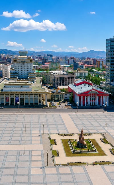 Ulaanbaatar's Sukhbaatar Square with government and theatre buildings, a central monument and mountains behind the city.