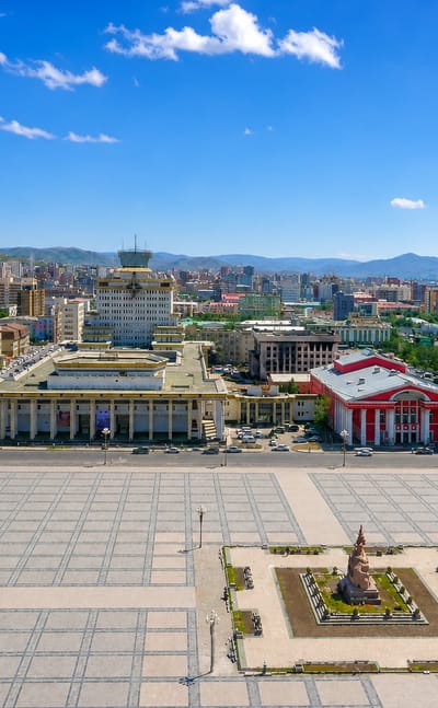 Sükhbaatar (Chinggis) Square with its equestrian statue, government buildings and glass tower in central Ulaanbaatar, mountains behind.