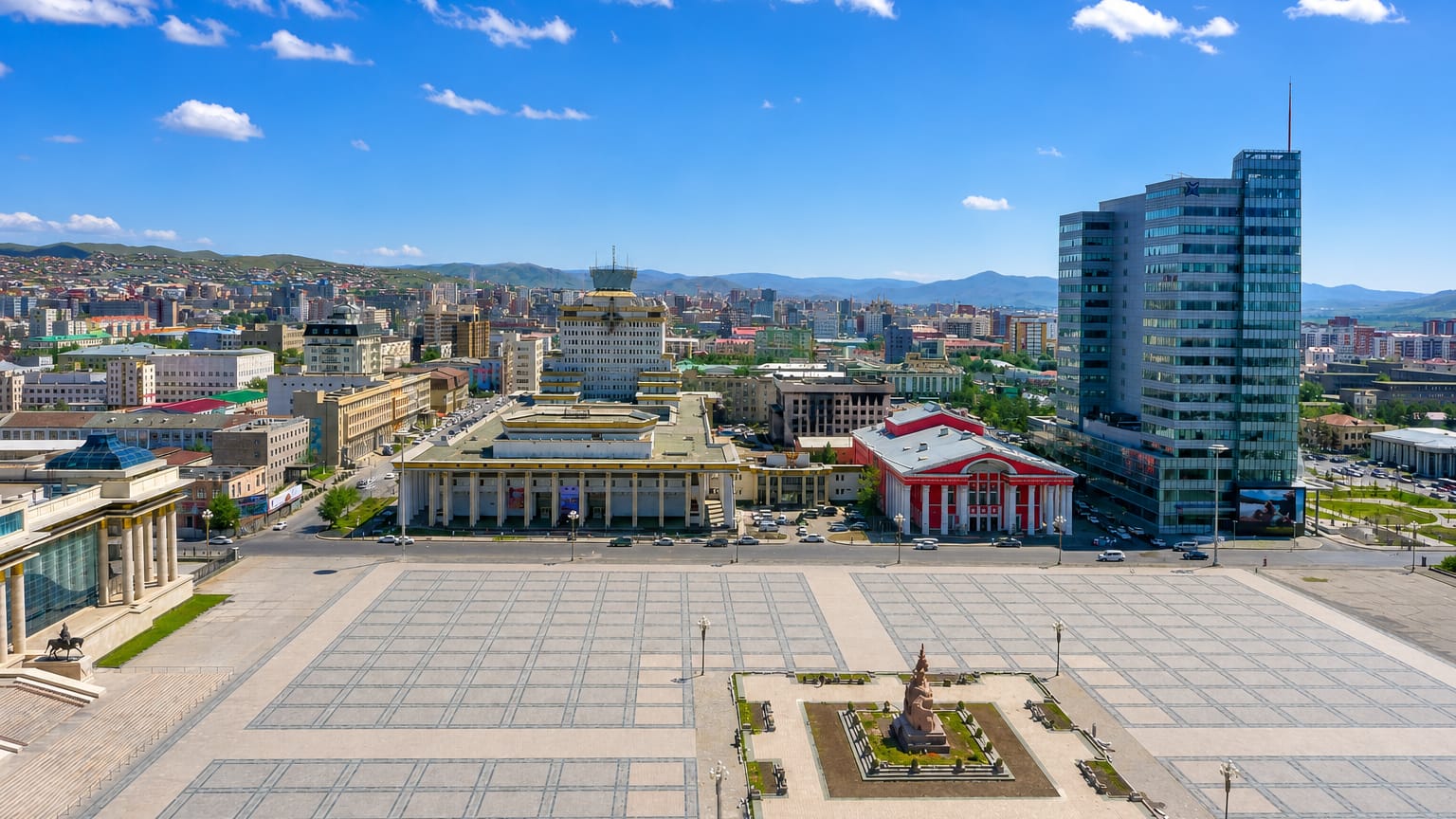 Sükhbaatar (Chinggis) Square with its equestrian statue, government buildings and glass tower in central Ulaanbaatar, mountains behind.