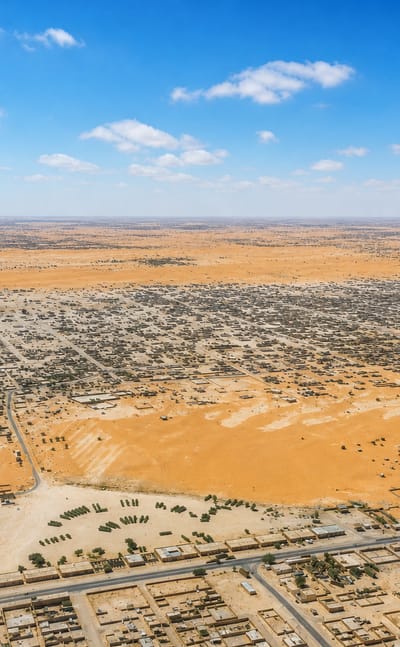 Aerial view of Nouakchott's low-rise sprawl spreading across the flat Saharan sands under a blue sky.