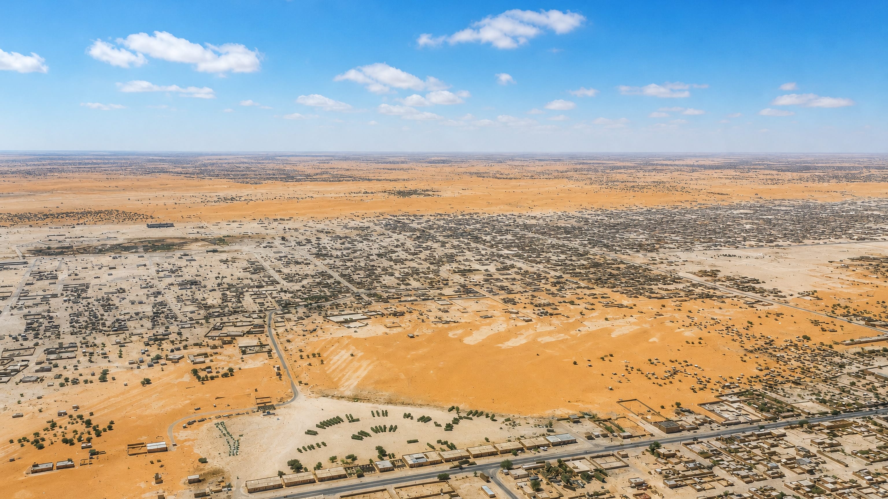 Aerial view of Nouakchott's low-rise sprawl spreading across the flat Saharan sands under a blue sky.