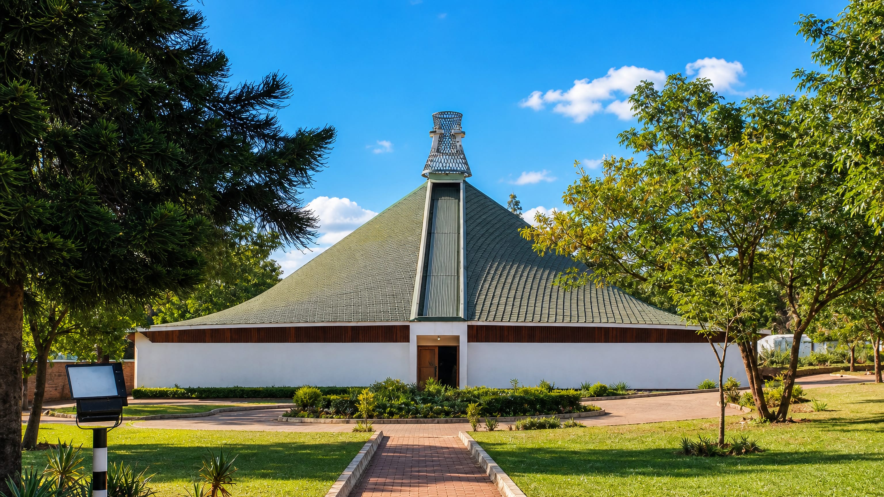 Modern church with a sweeping conical roof and lattice spire set in green gardens in Blantyre, Malawi.
