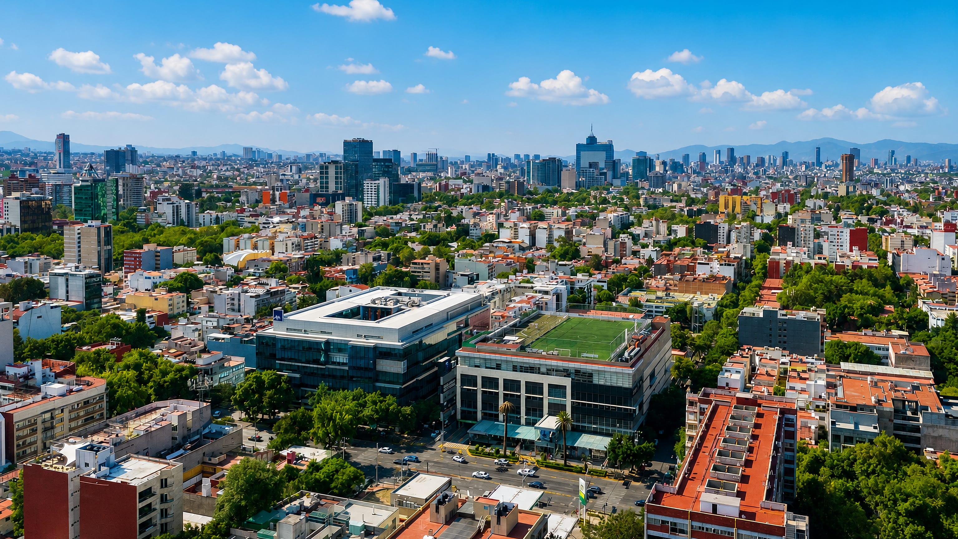 Leafy mid-rise blocks of Colonia del Valle with Mexico City's skyline and mountains beyond.