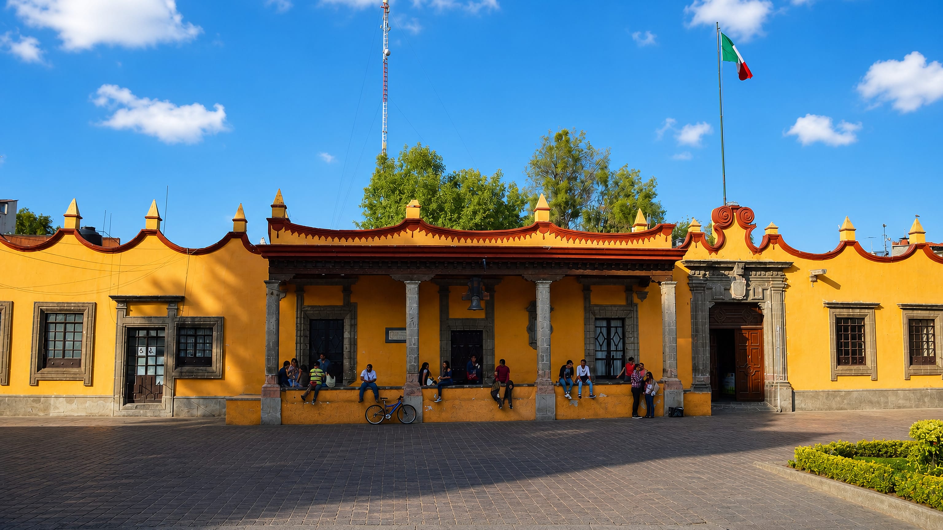 Coyoacán's ochre Casa Municipal on Plaza Hidalgo in Mexico City, with a Mexican flag above the colonnade.