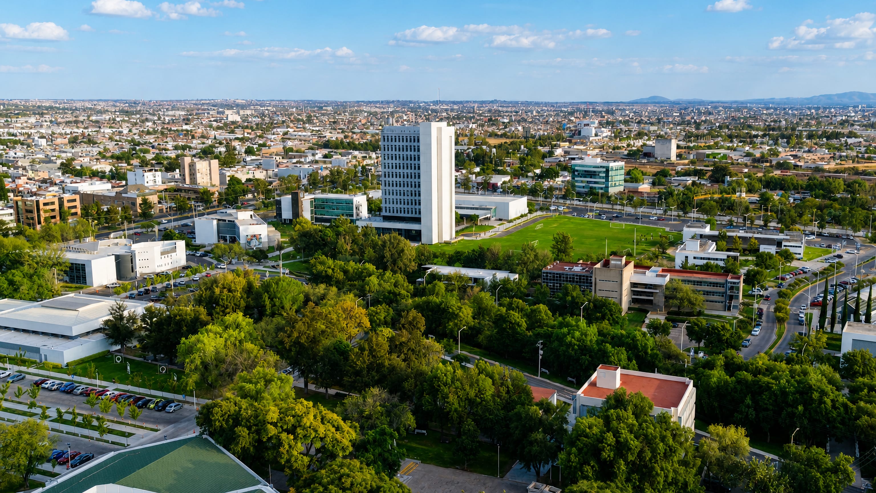 Green campus grounds and a white modernist tower from the air, with Aguascalientes stretching to distant hills.