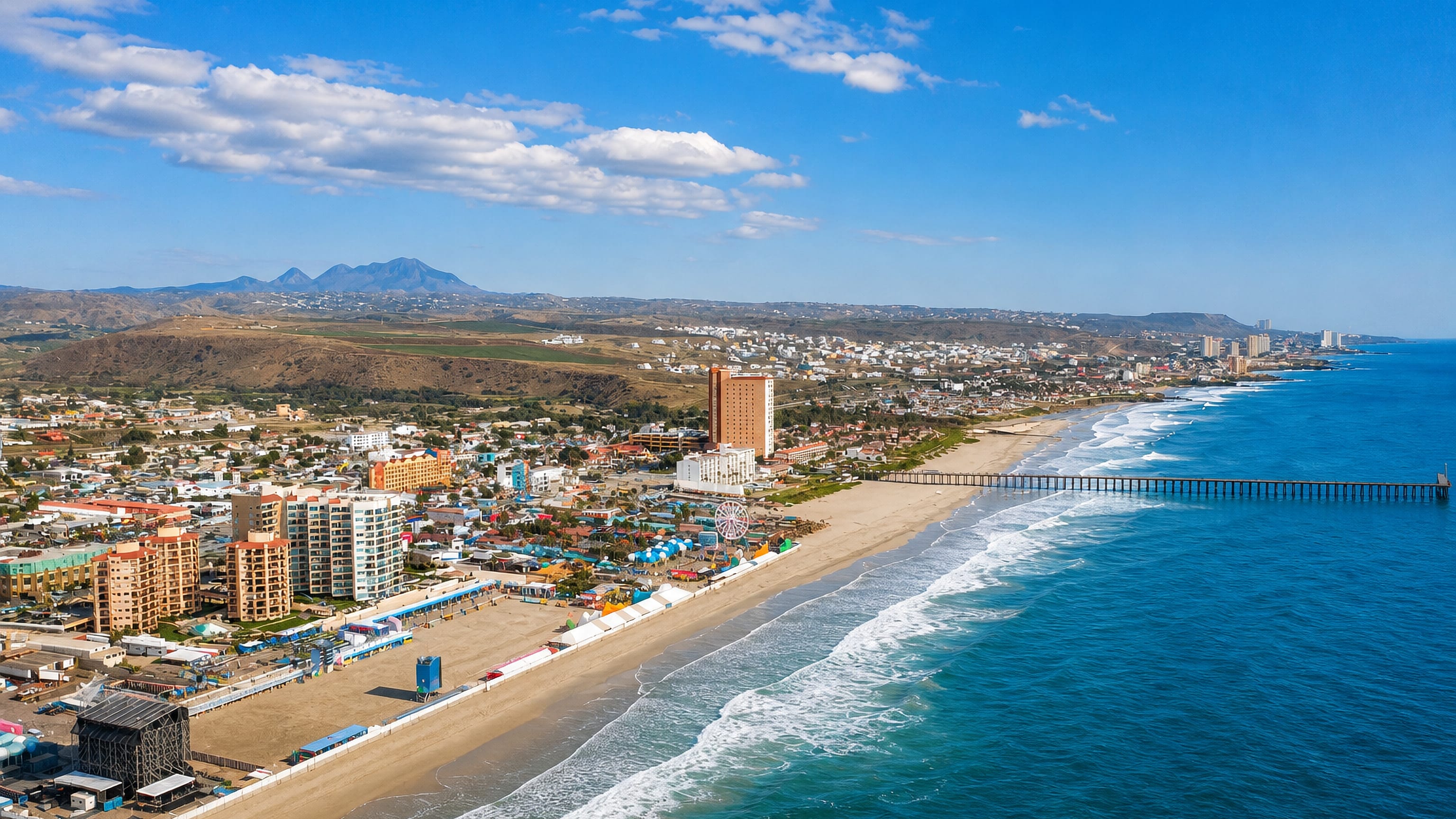 Aerial view of Rosarito, Baja California, its long Pacific beach, pier and beachfront hotels below coastal hills.