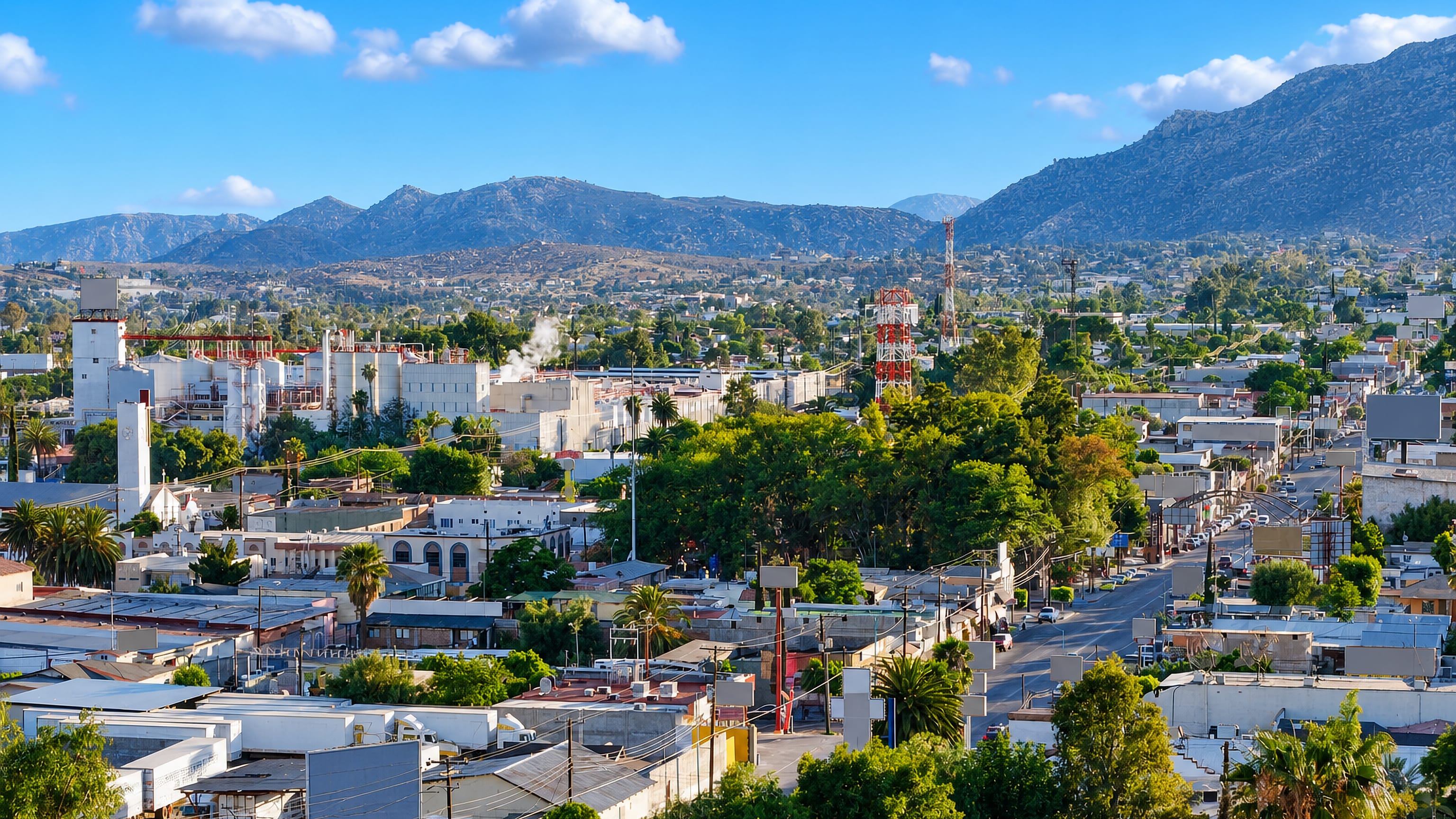 Daytime view over Tecate's low-rise streets and hillside brewery complex, with the Baja California sierra behind.