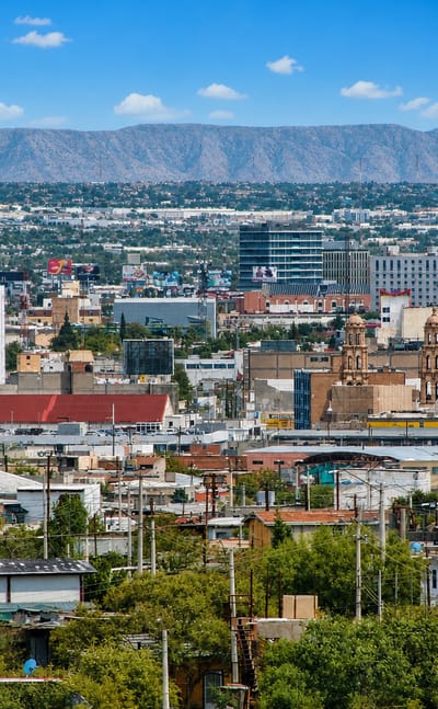 Sprawling Ciudad Juarez rooftops with a twin-towered church and desert mountains on the horizon.