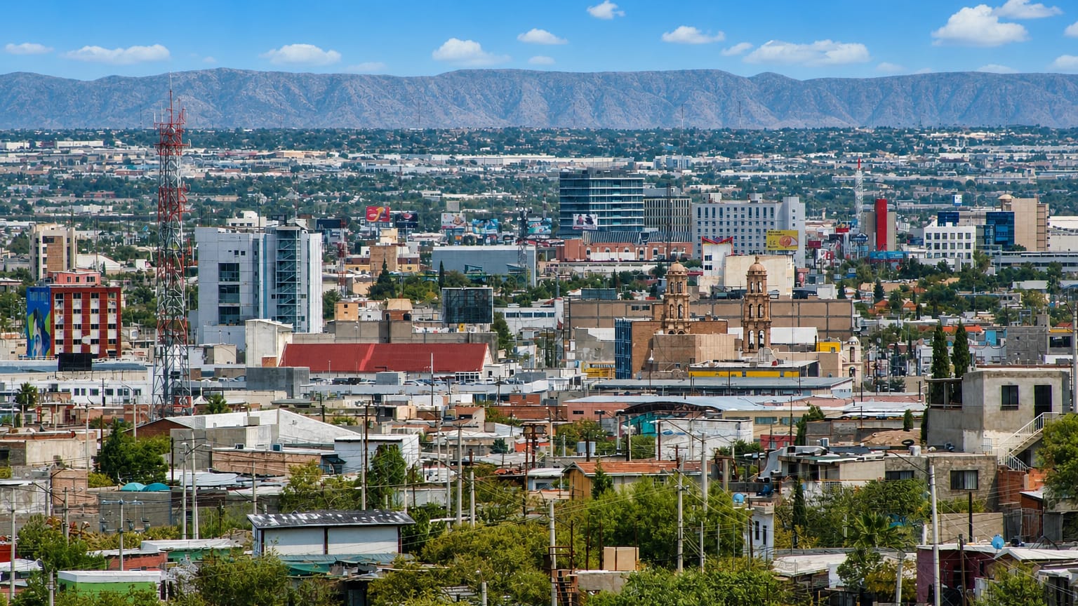 Sprawling Ciudad Juarez rooftops with a twin-towered church and desert mountains on the horizon.