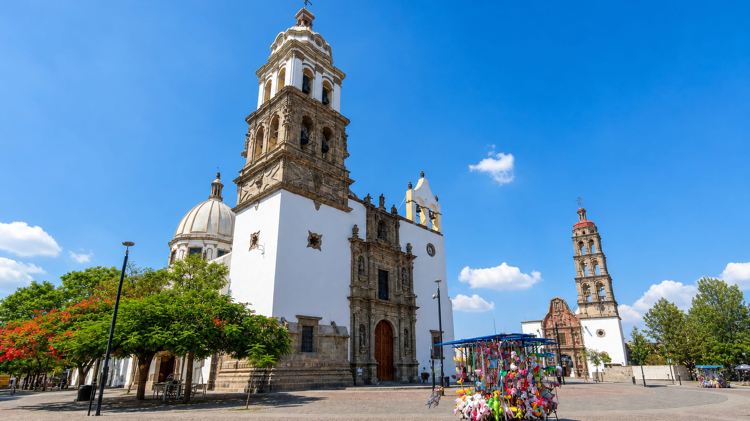 Baroque church towers over the paved main plaza in Irapuato, Mexico, with a balloon vendor's cart.