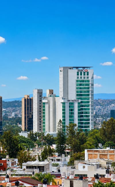 Guadalajara business district with HSBC and NH Hoteles towers over tiled-roof neighborhoods and distant hills