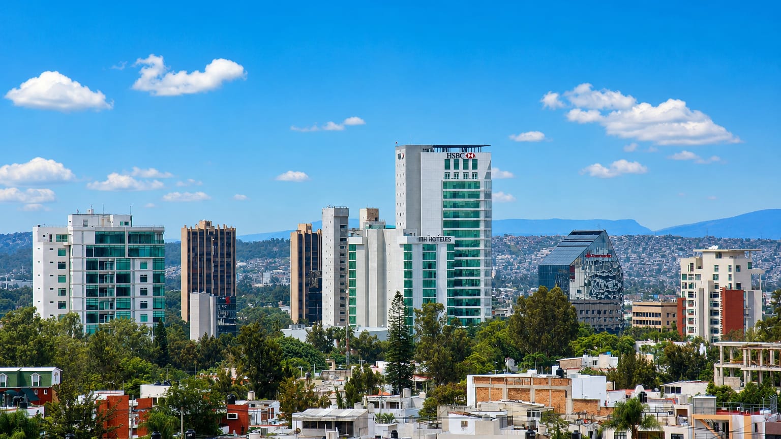 Guadalajara business district with HSBC and NH Hoteles towers over tiled-roof neighborhoods and distant hills