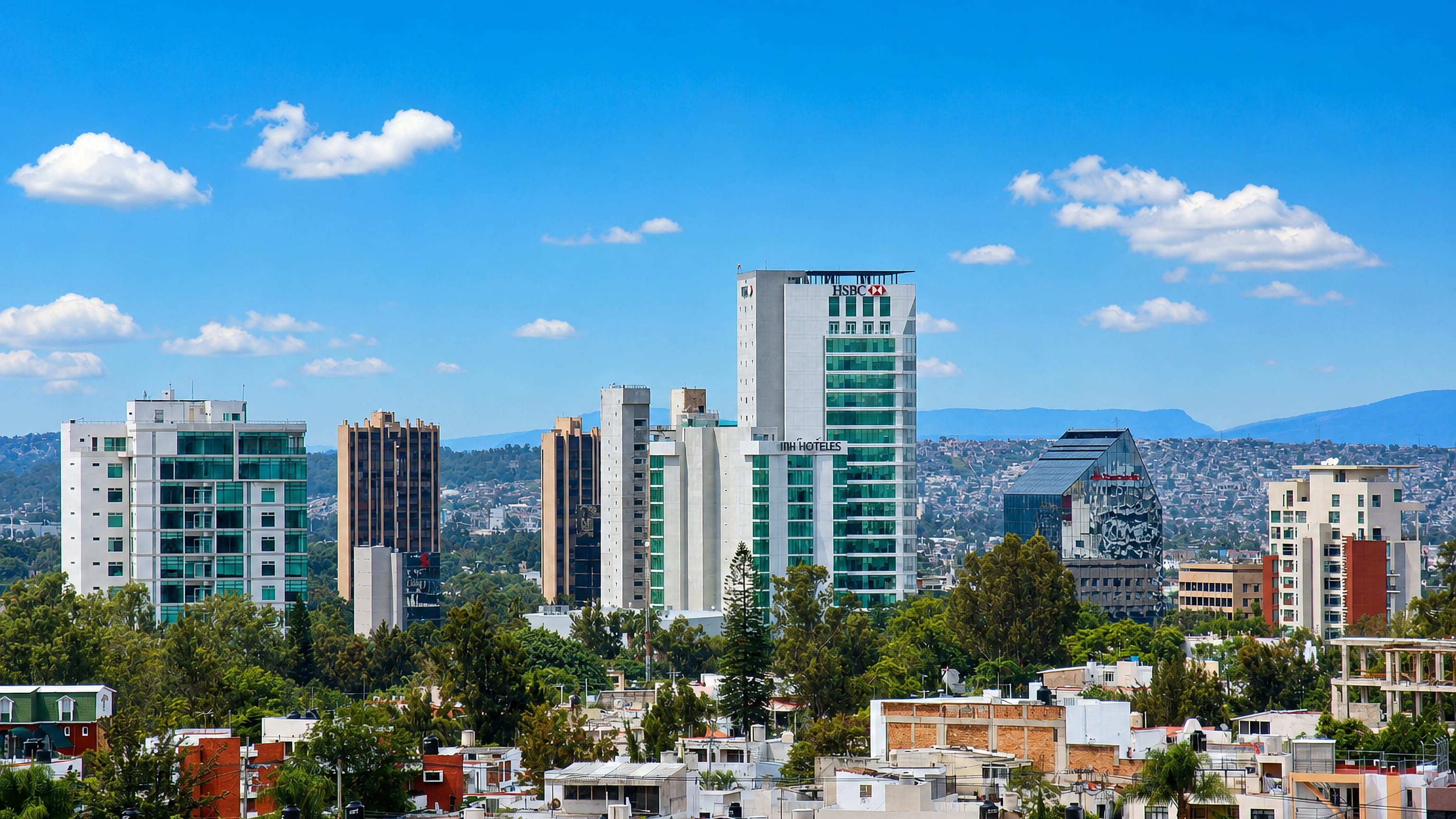 Guadalajara business district with HSBC and NH Hoteles towers over tiled-roof neighborhoods and distant hills