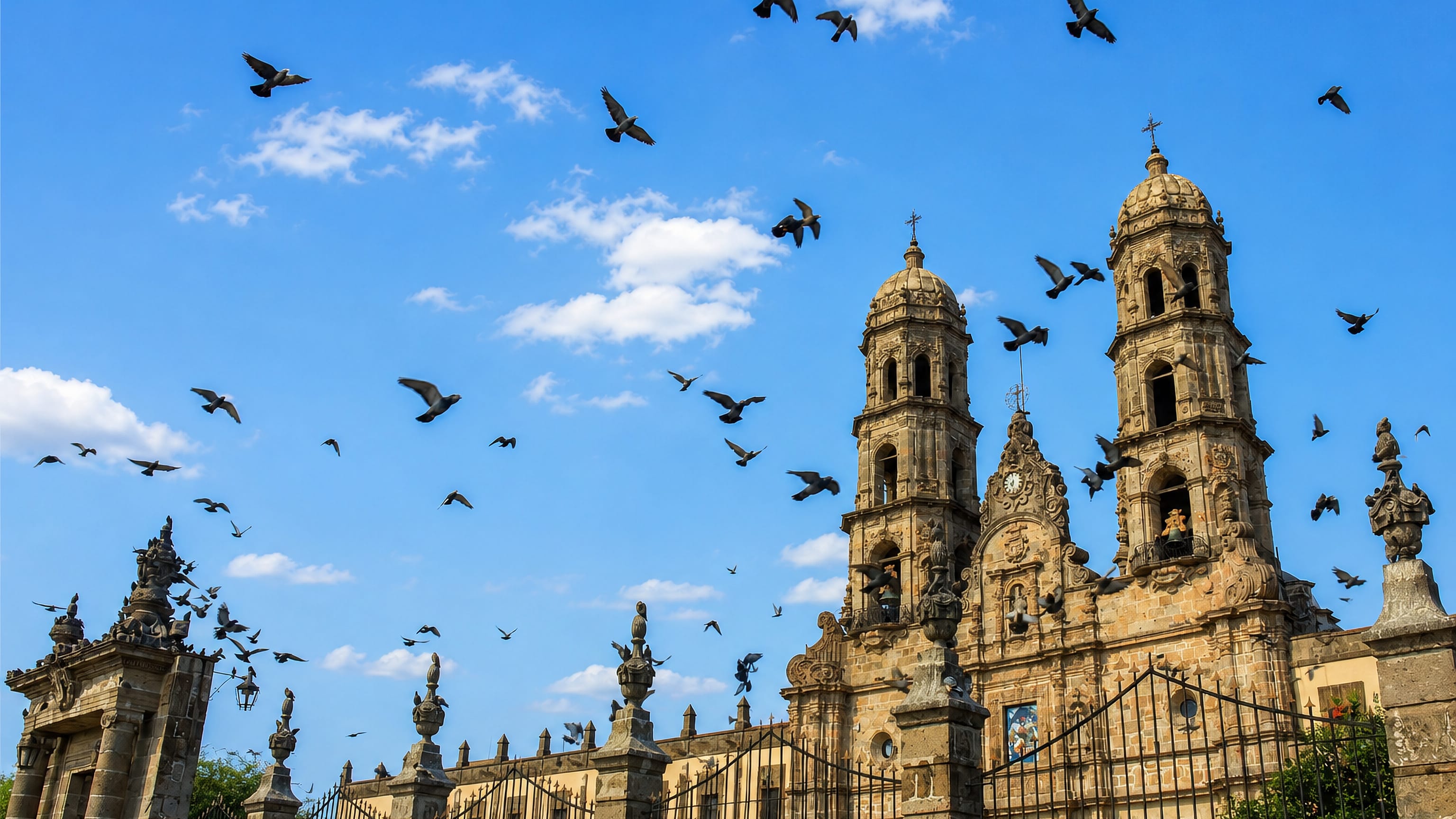 Twin baroque towers of the Basilica of Our Lady of Zapopan under a blue sky with pigeons wheeling, Jalisco.