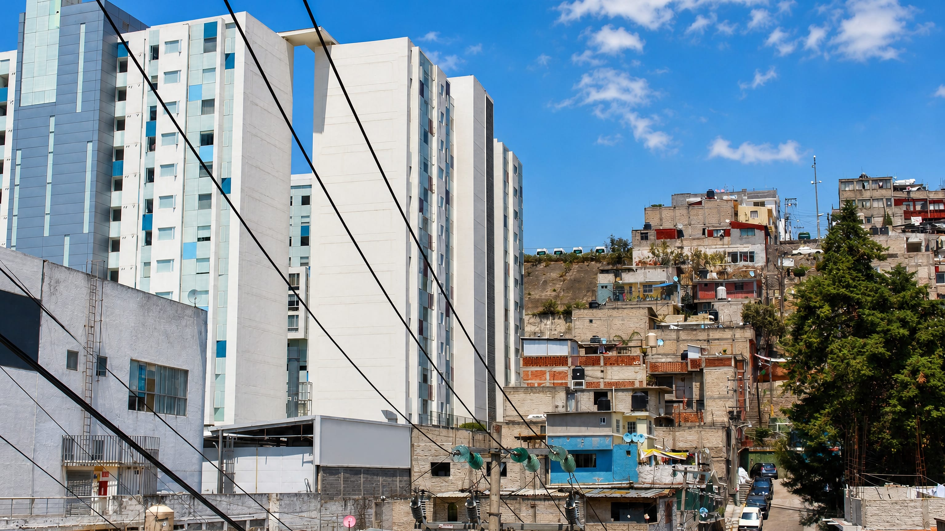 New white apartment towers rising beside dense hillside housing in Huixquilucan, Estado de México.