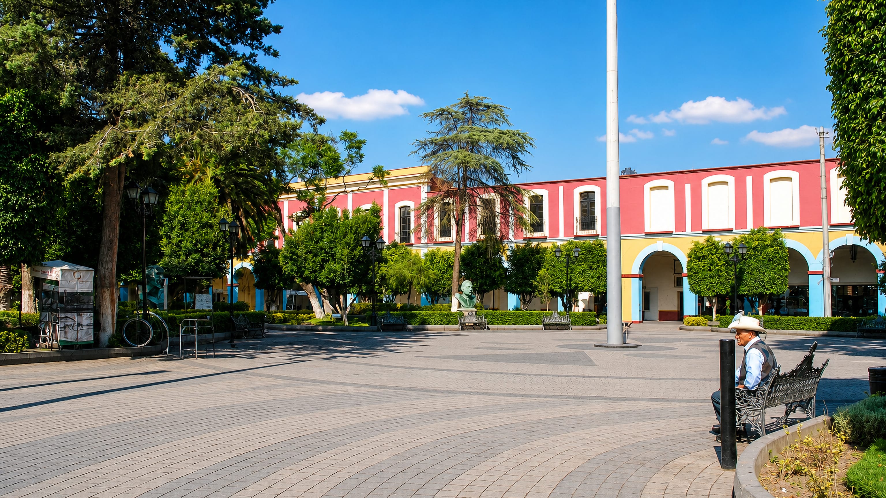 Arcaded pink and yellow portales lining the tree-shaded main plaza of Texcoco de Mora, Mexico.
