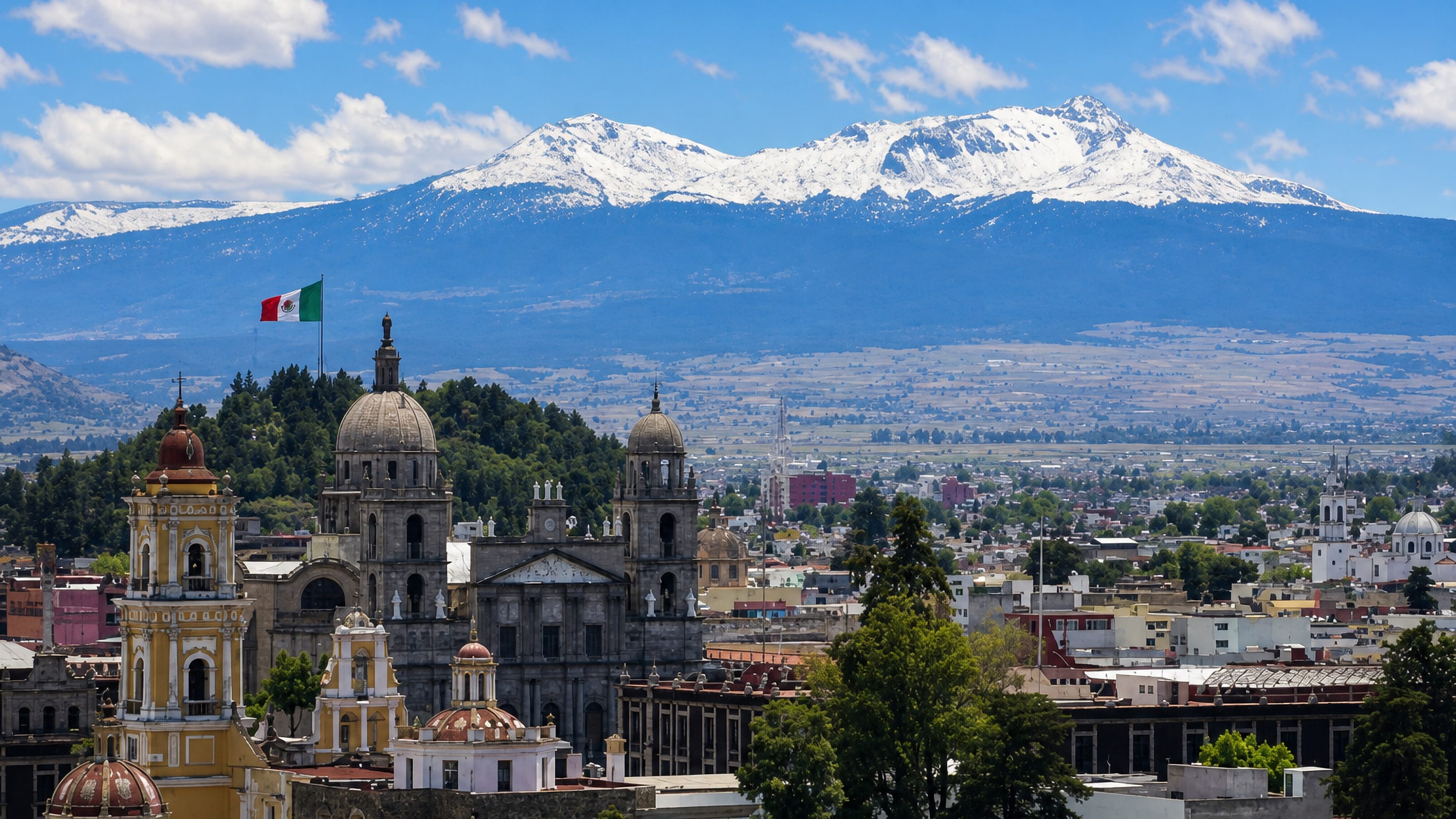 Toluca's cathedral domes and bell towers below the snow-capped Nevado de Toluca, with a Mexican flag over the centre.